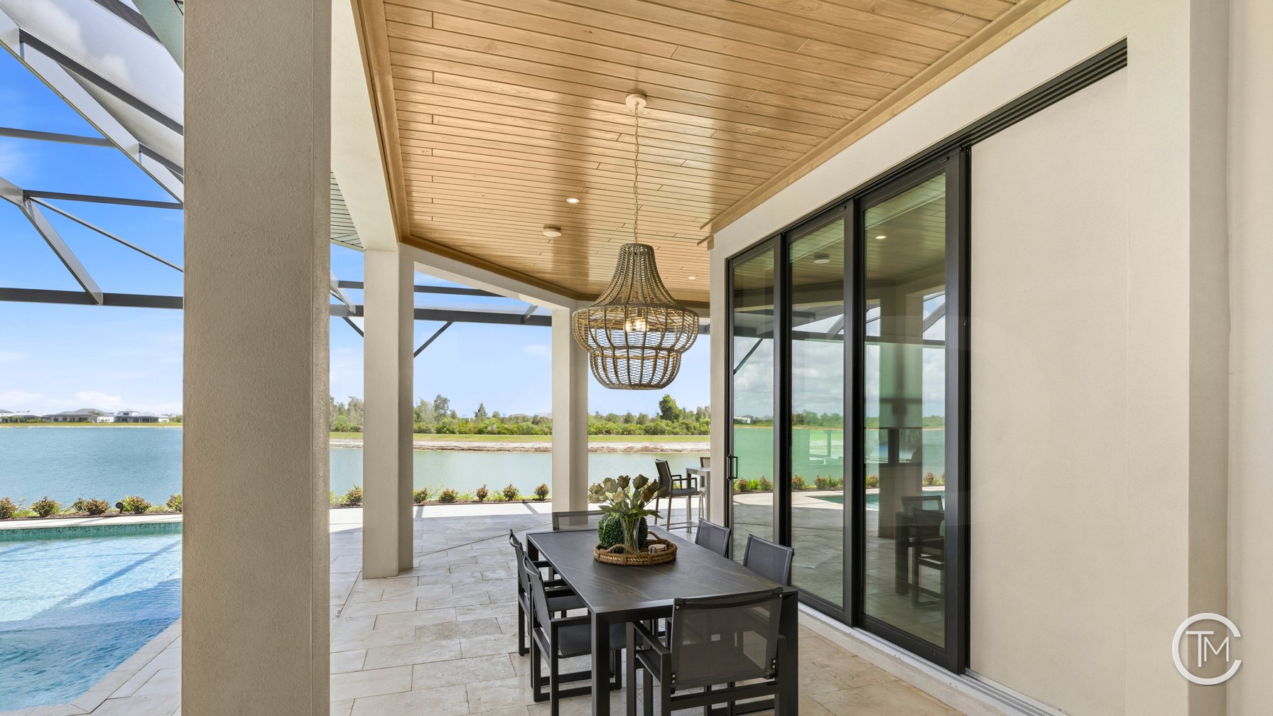 Covered lanai with a honey-toned tongue-and-groove wood ceiling, a woven pendant over an outdoor dining table and a screened pool beyond